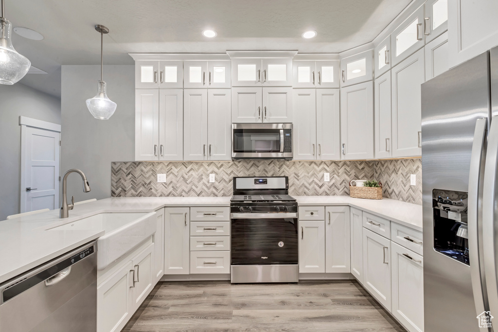 Kitchen featuring light hardwood / wood-style floors, stainless steel appliances, white cabinets, pendant lighting, and sink