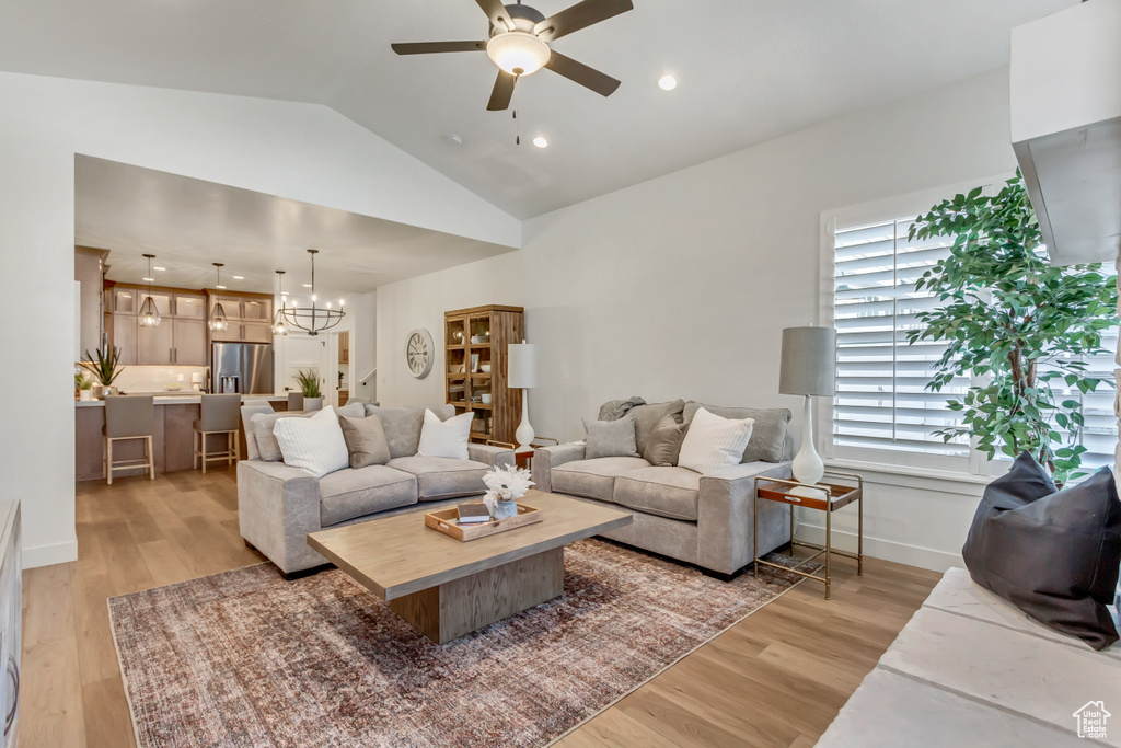 Living room featuring light hardwood / wood-style floors, ceiling fan with notable chandelier, and lofted ceiling