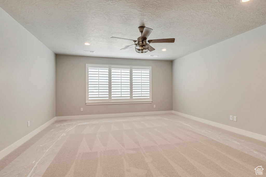 Carpeted empty room featuring a textured ceiling and ceiling fan