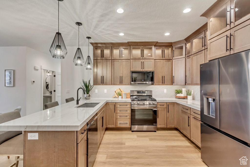 Kitchen with stainless steel appliances, decorative light fixtures, sink, a breakfast bar, and light hardwood / wood-style flooring