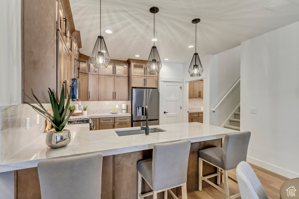 Kitchen with stainless steel refrigerator with ice dispenser, backsplash, light stone countertops, pendant lighting, and light hardwood / wood-style flooring