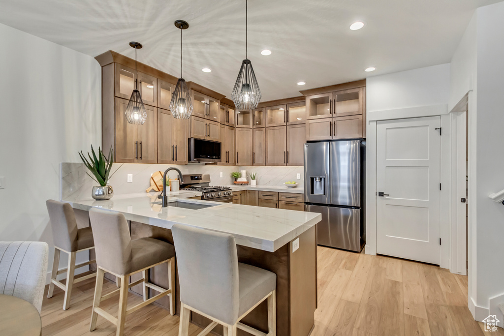 Kitchen with pendant lighting, kitchen peninsula, light hardwood / wood-style floors, and stainless steel appliances