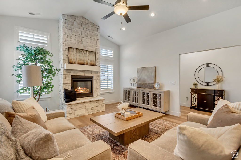 Living room with a stone fireplace, light wood-type flooring, vaulted ceiling, and ceiling fan