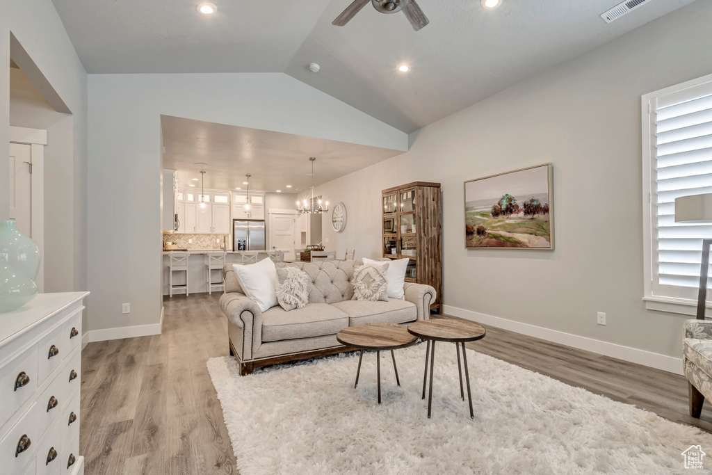 Living room featuring vaulted ceiling, ceiling fan with notable chandelier, and light hardwood / wood-style flooring