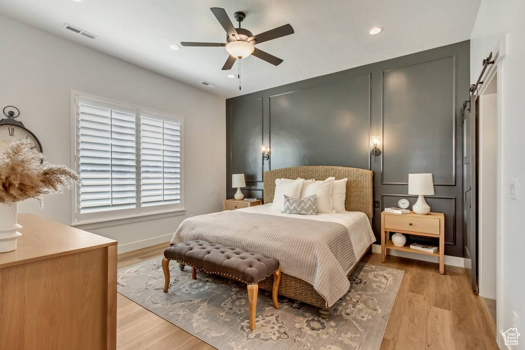 Bedroom with a barn door, light hardwood / wood-style floors, and ceiling fan