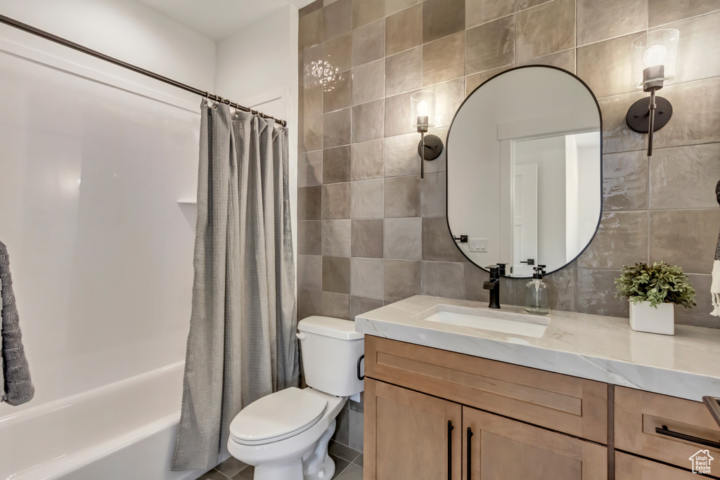 Full bathroom featuring toilet, tile walls, tile patterned flooring, vanity, and shower / bath combination with curtain