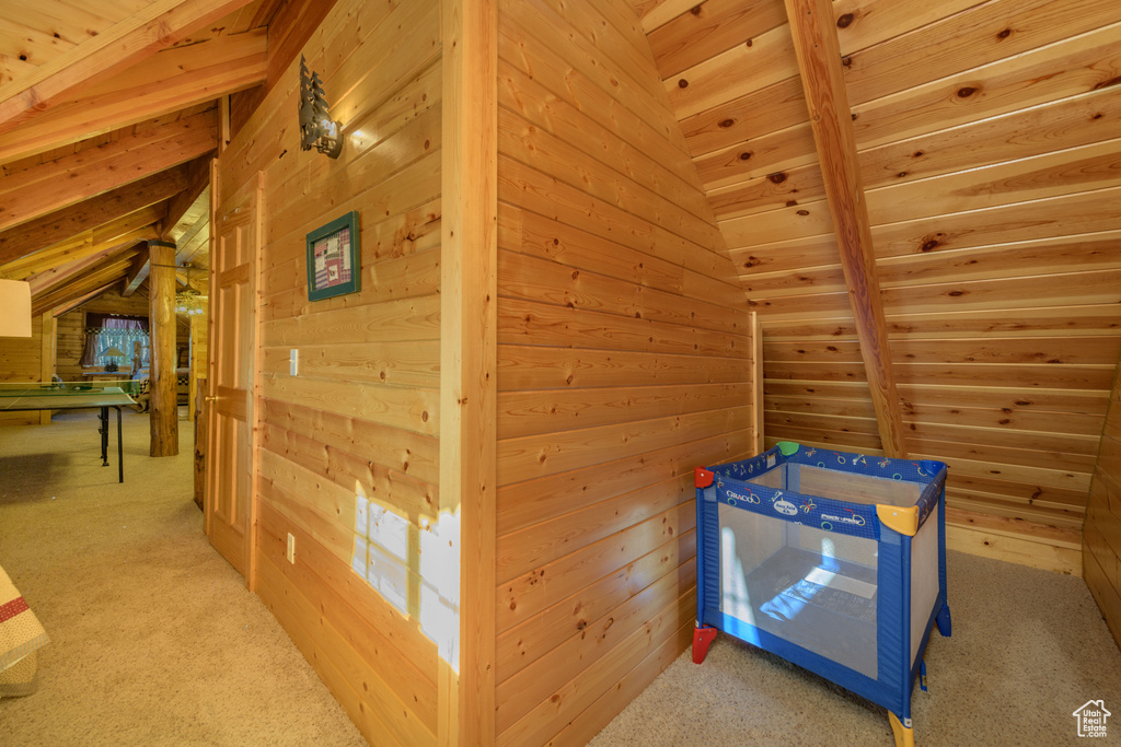 Carpeted bedroom with wooden ceiling, lofted ceiling with beams, and wood walls