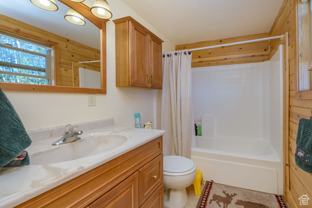 Full bathroom with wooden walls, shower / bath combination with curtain, toilet, and large vanity