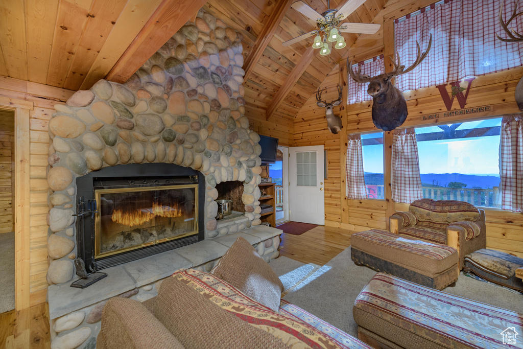 Living room with vaulted ceiling with beams, a mountain view, wooden ceiling, hardwood / wood-style flooring, and a stone fireplace