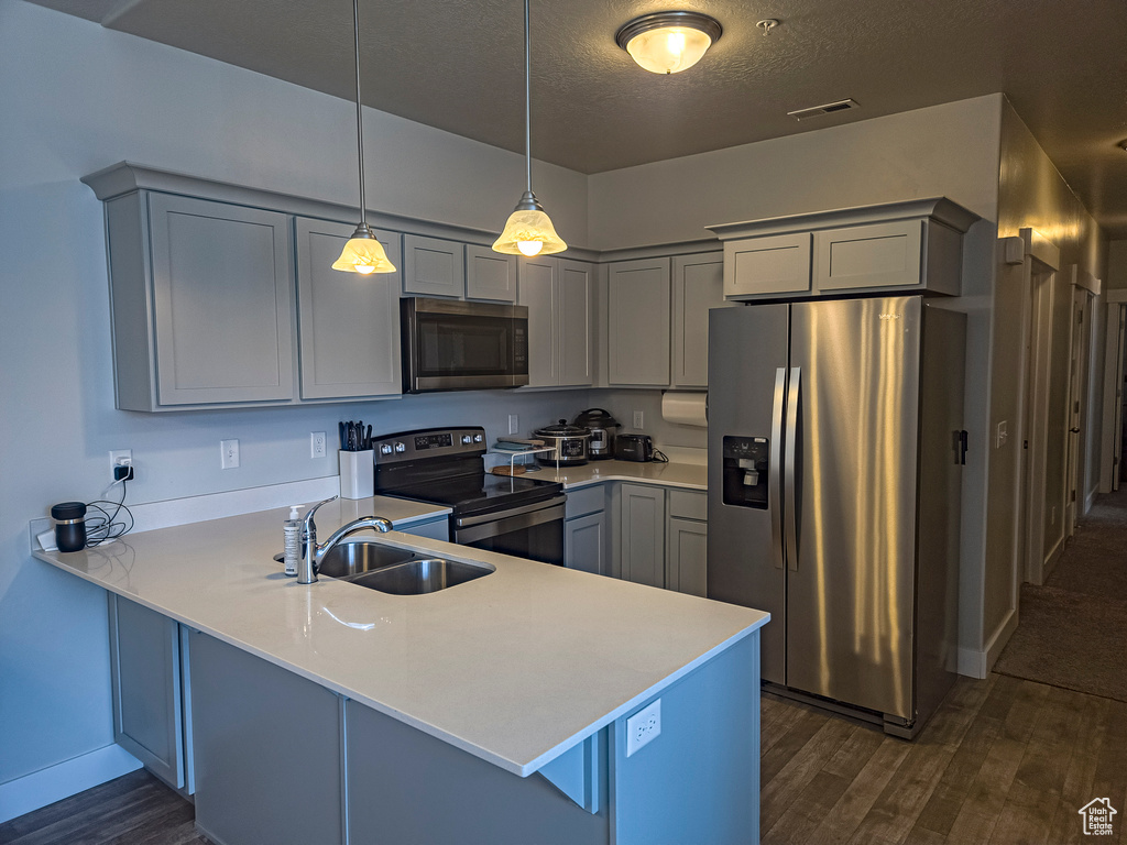 Kitchen featuring kitchen peninsula, dark carpet, hanging light fixtures, sink, and appliances with stainless steel finishes