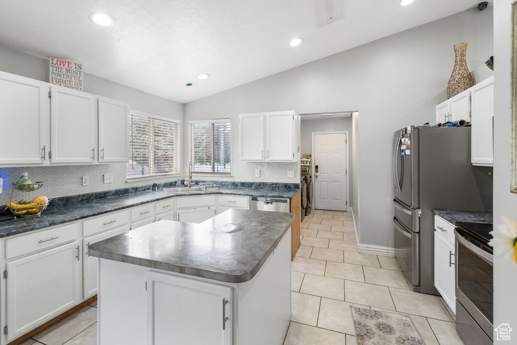 Kitchen with backsplash, vaulted ceiling, appliances with stainless steel finishes, and a kitchen island