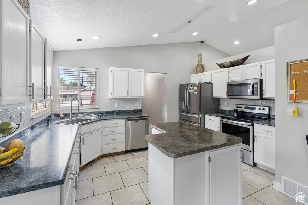 Kitchen featuring a kitchen island, lofted ceiling, white cabinets, sink, and appliances with stainless steel finishes