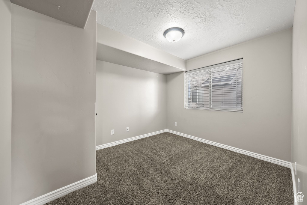 Empty room featuring dark colored carpet and a textured ceiling