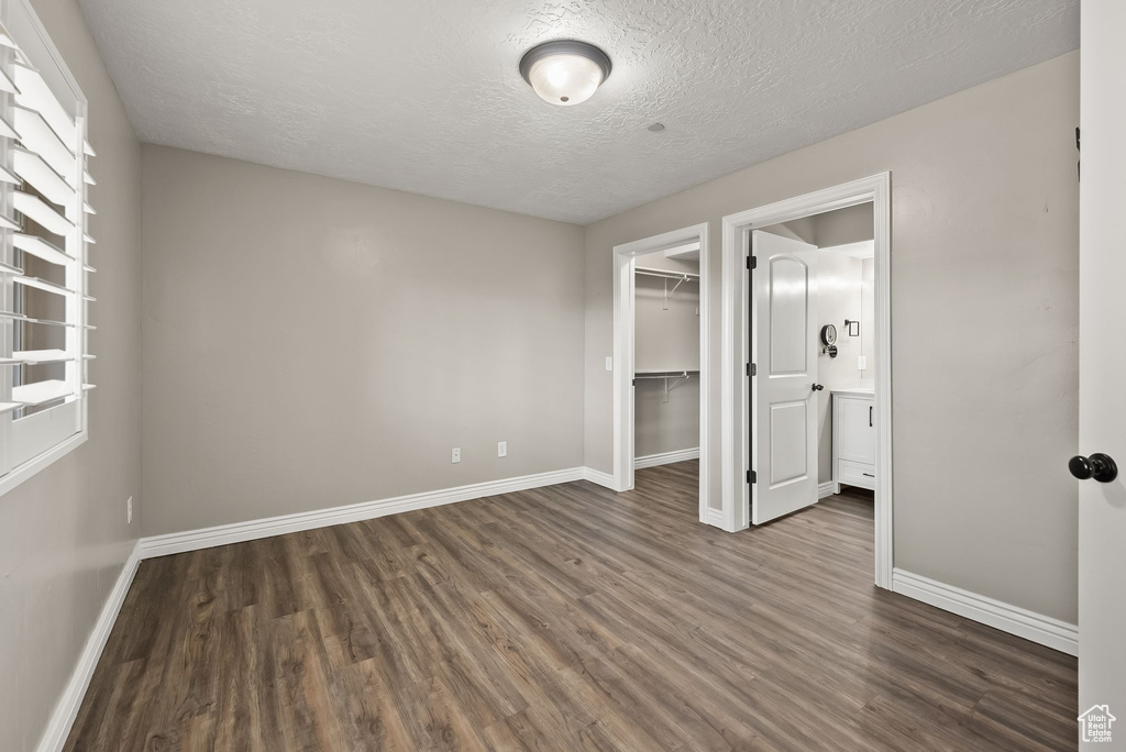 Unfurnished bedroom featuring a closet, dark hardwood / wood-style flooring, a textured ceiling, and a spacious closet