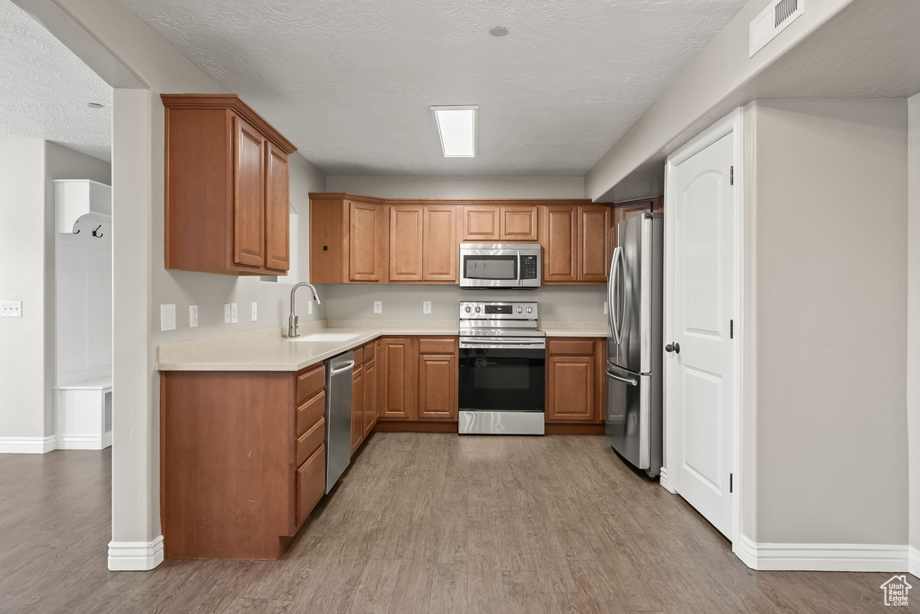 Kitchen featuring appliances with stainless steel finishes, sink, light hardwood / wood-style flooring, and a textured ceiling