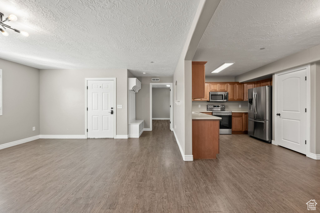 Kitchen with dark wood-type flooring, appliances with stainless steel finishes, a textured ceiling, and kitchen peninsula