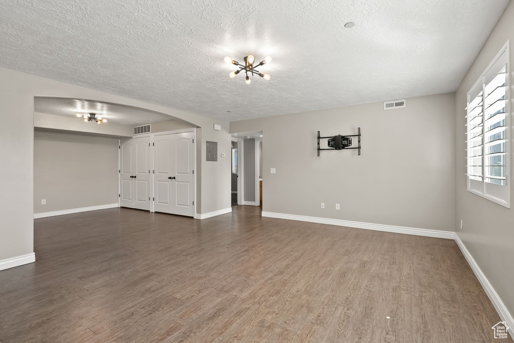 Unfurnished living room with a textured ceiling, a notable chandelier, and hardwood / wood-style floors