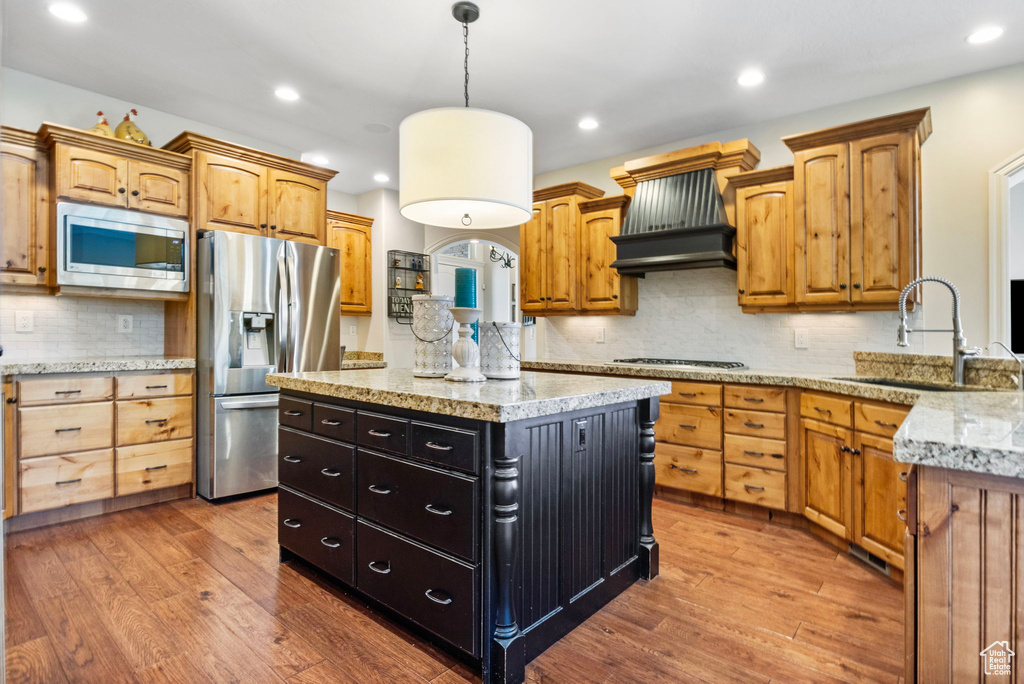 Kitchen with pendant lighting, wood-type flooring, backsplash, a center island, and appliances with stainless steel finishes