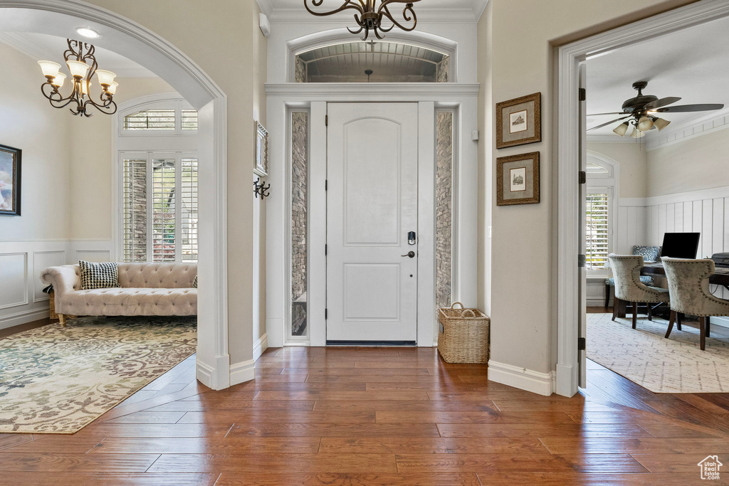 Entryway featuring ornamental molding, ceiling fan with notable chandelier, and dark wood-type flooring