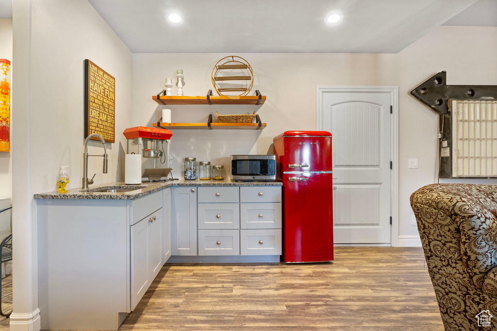 Kitchen with sink, stone counters, light wood-type flooring, and refrigerator