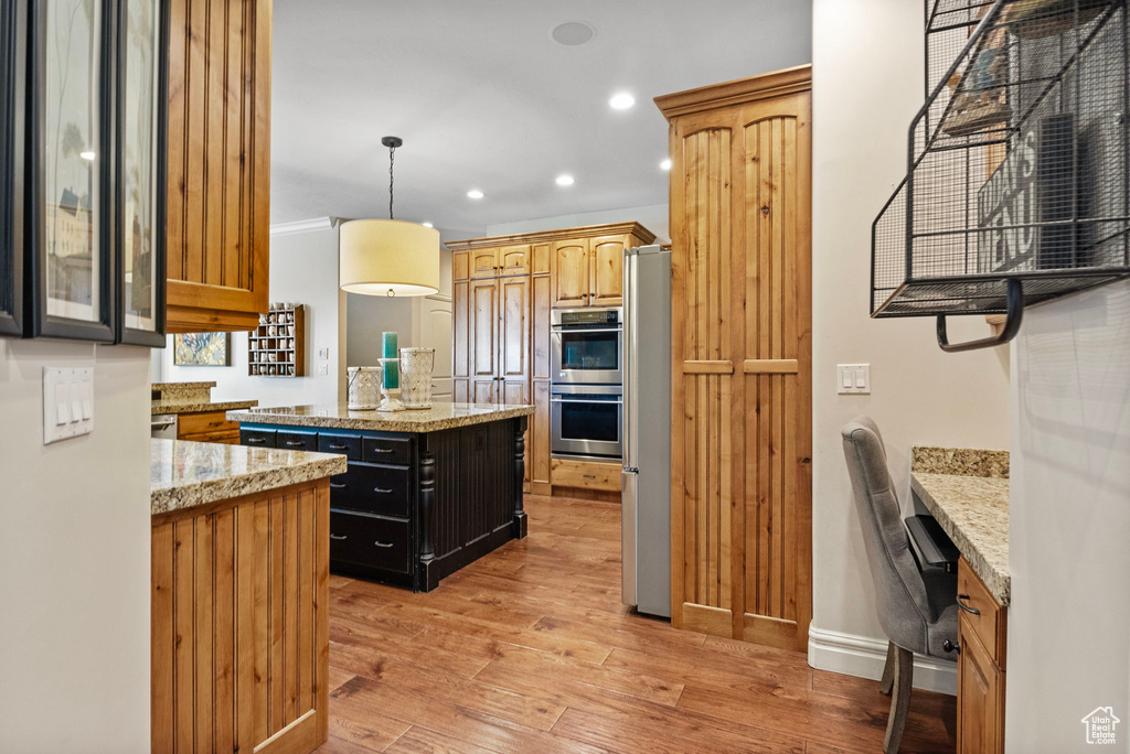 Kitchen with light hardwood / wood-style flooring, stainless steel appliances, pendant lighting, light stone counters, and a center island