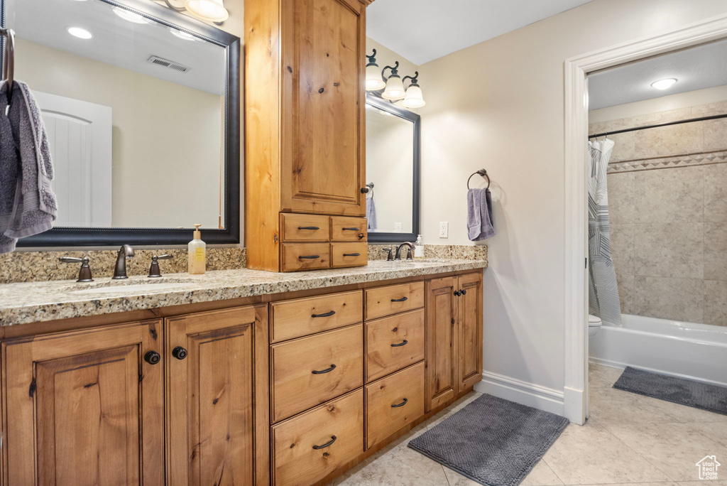 Full bathroom with dual sinks, vanity with extensive cabinet space, shower / tub combo, tile floors, and toilet