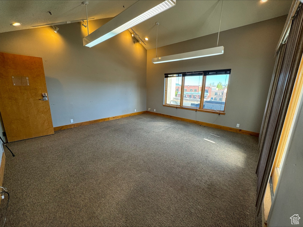 Carpeted empty room featuring high vaulted ceiling and rail lighting