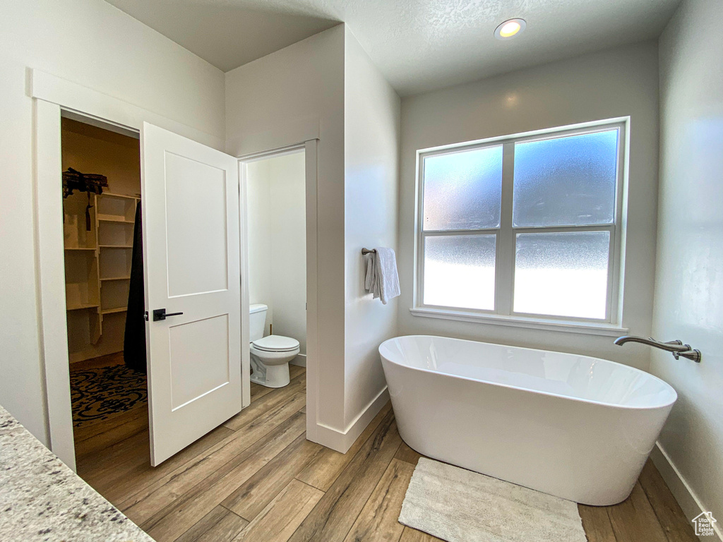 Bathroom with plenty of natural light, a washtub, toilet, and hardwood / wood-style floors