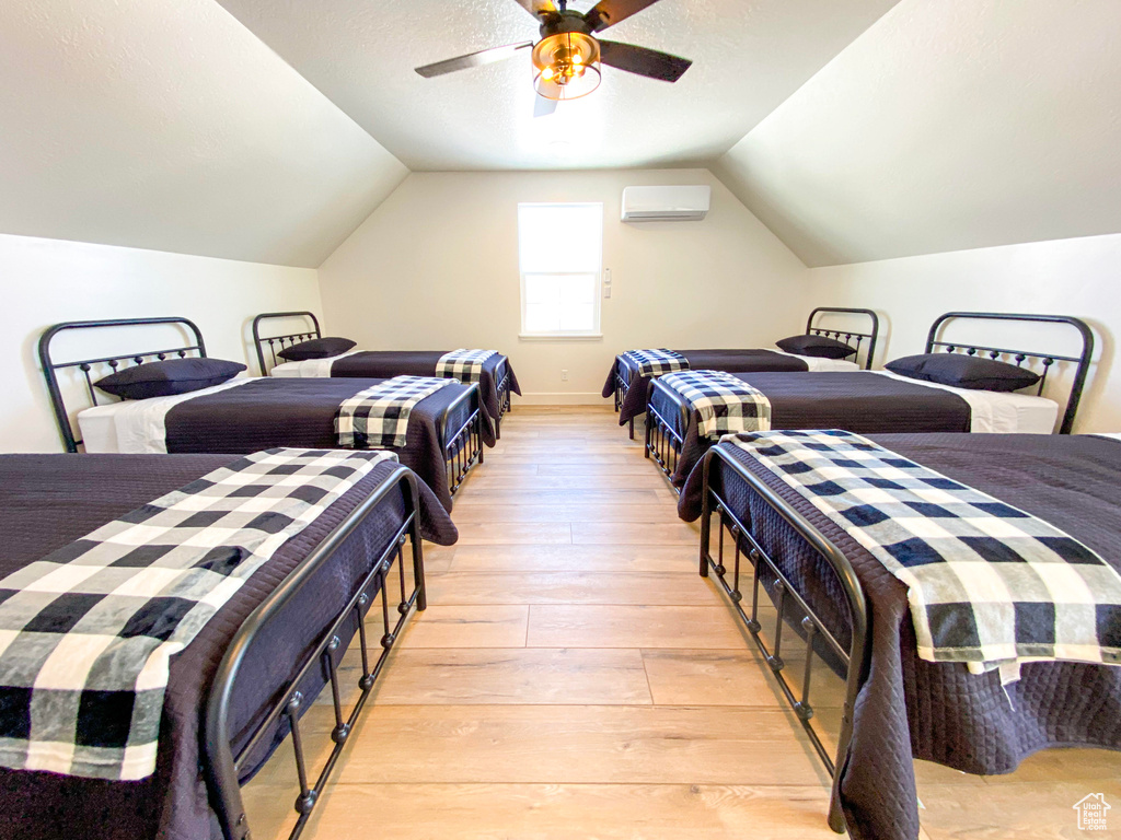 Bedroom featuring ceiling fan, light hardwood / wood-style flooring, vaulted ceiling, and an AC wall unit