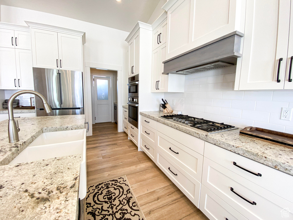 Kitchen with appliances with stainless steel finishes, light hardwood / wood-style floors, white cabinets, and backsplash