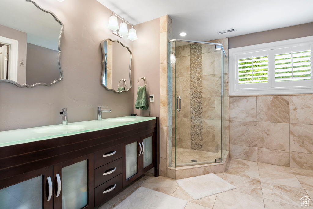 Bathroom with double vanity, a shower with shower door, and tile floors