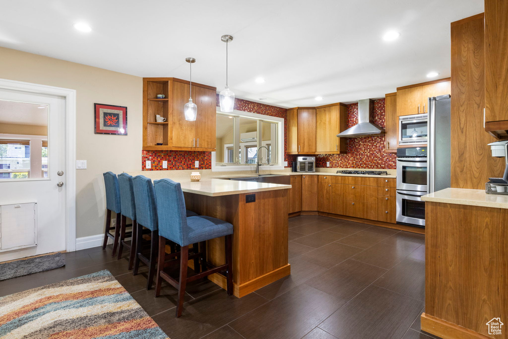 Kitchen featuring hanging light fixtures, wall chimney exhaust hood, stainless steel appliances, and backsplash