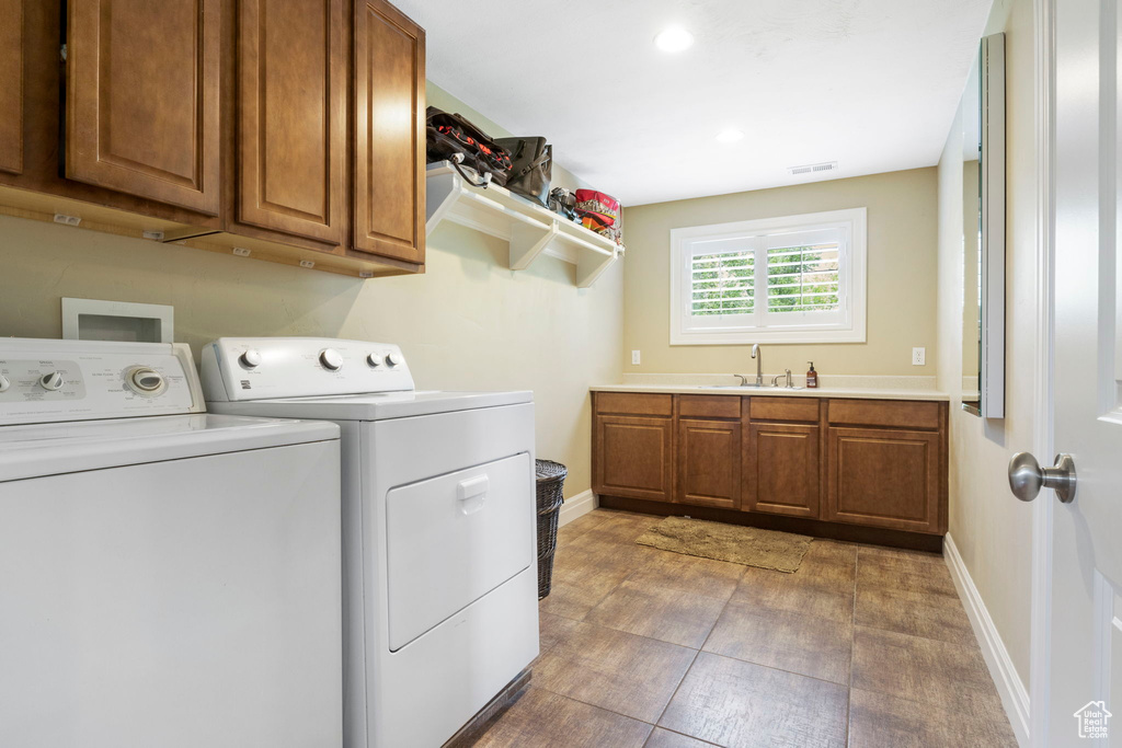 Clothes washing area with cabinets, tile flooring, washing machine and clothes dryer, hookup for a washing machine, and sink