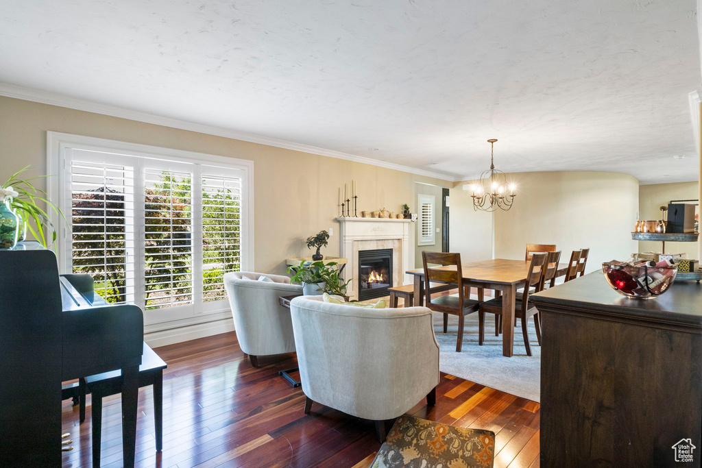 Living room with a notable chandelier, a tiled fireplace, crown molding, and dark wood-type flooring