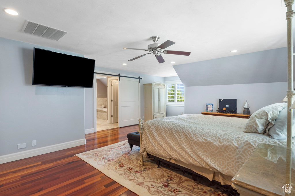 Bedroom with ceiling fan, vaulted ceiling, a barn door, ensuite bathroom, and hardwood / wood-style flooring