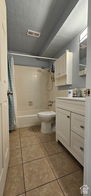 Full bathroom featuring toilet, tile floors, shower / bath combo with shower curtain, vanity, and a textured ceiling