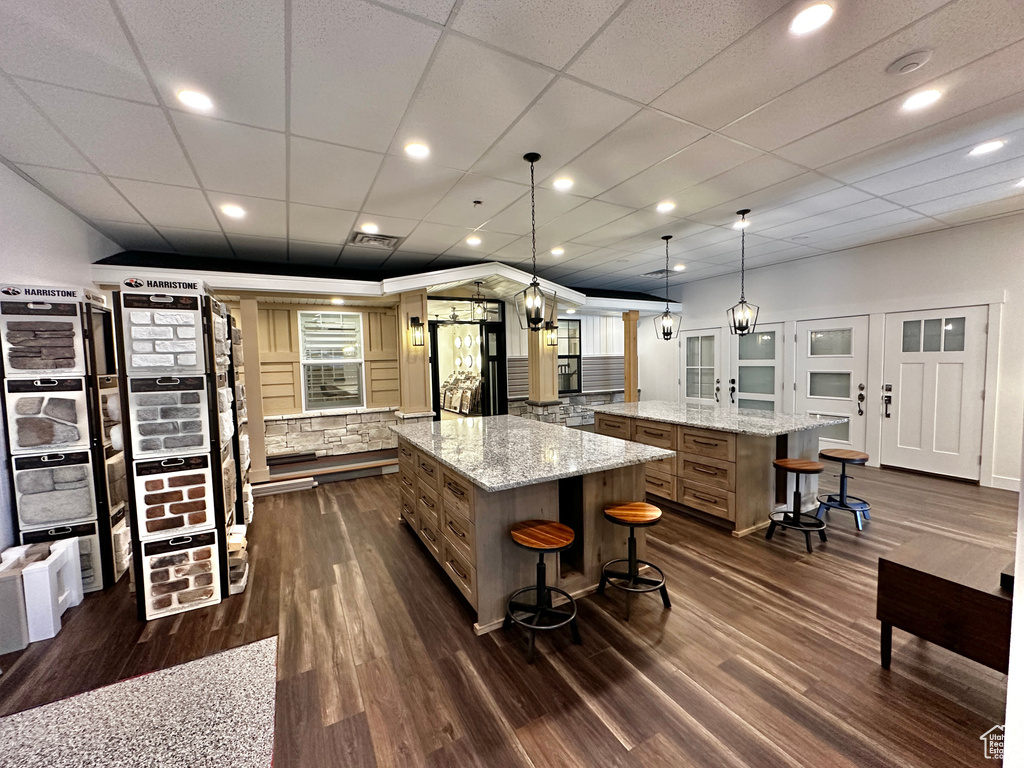 Kitchen with dark wood-type flooring, light stone counters, a large island, pendant lighting, and a breakfast bar