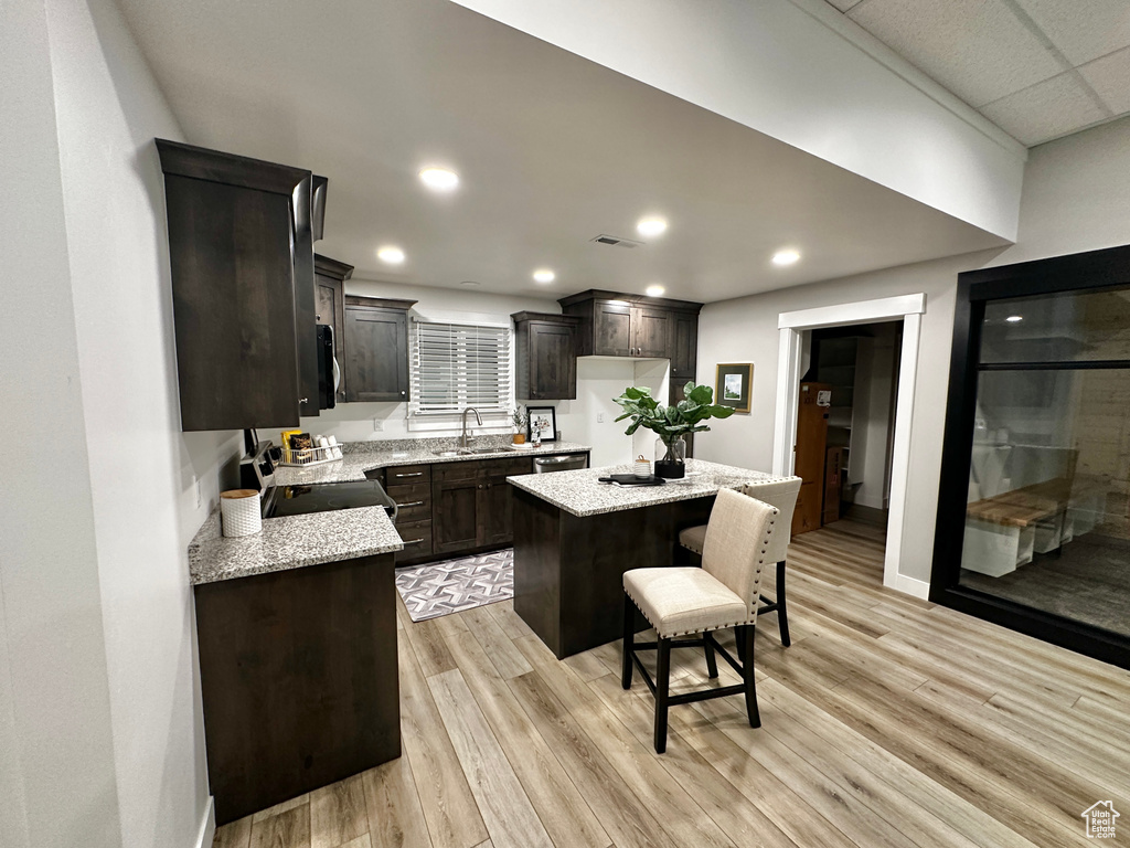 Kitchen featuring light stone countertops, light hardwood / wood-style flooring, stainless steel range with electric cooktop, dark brown cabinetry, and a kitchen island