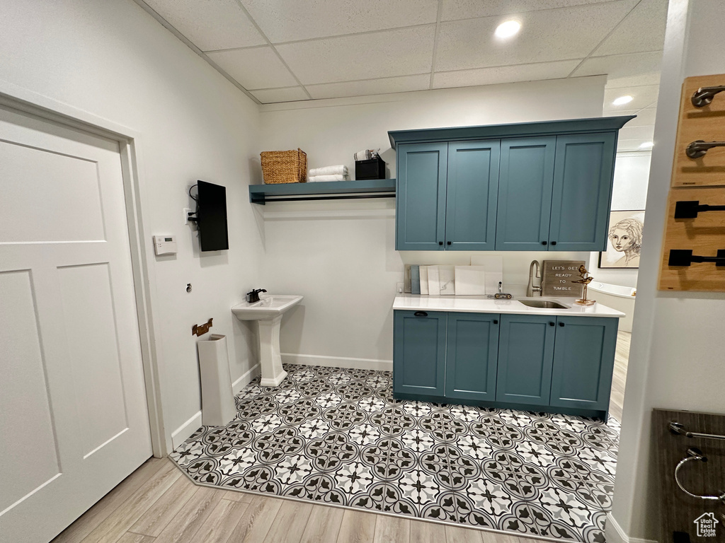 Interior space with blue cabinetry, a paneled ceiling, sink, and light tile flooring