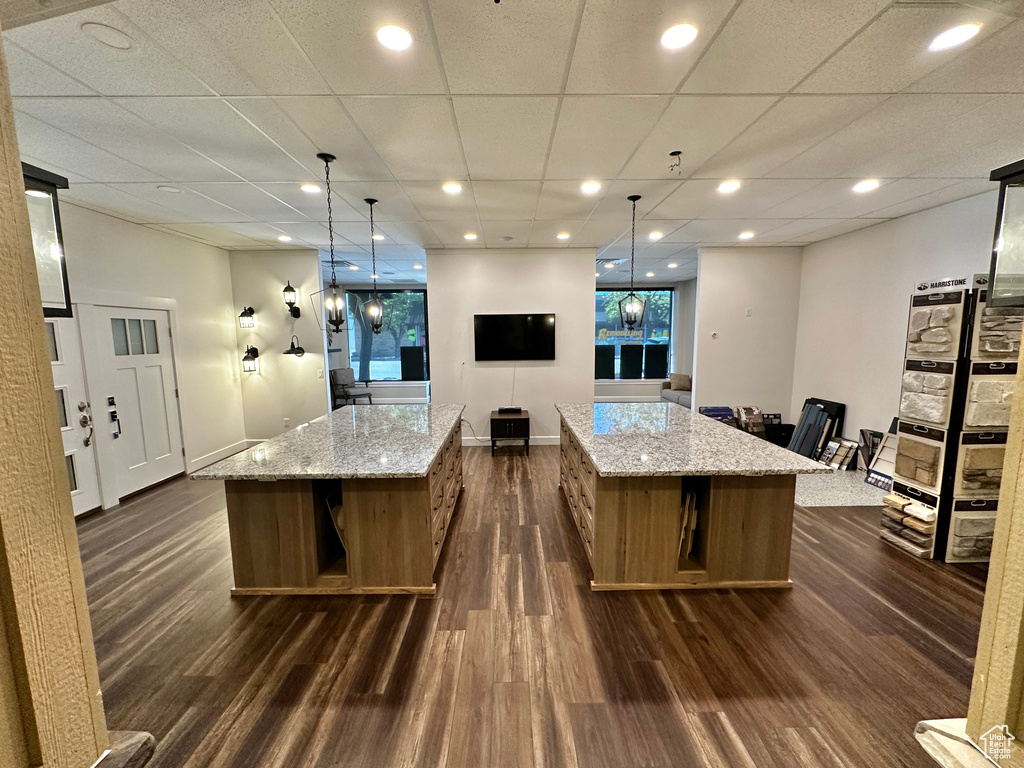 Kitchen with dark wood-type flooring, light stone countertops, a large island, and pendant lighting