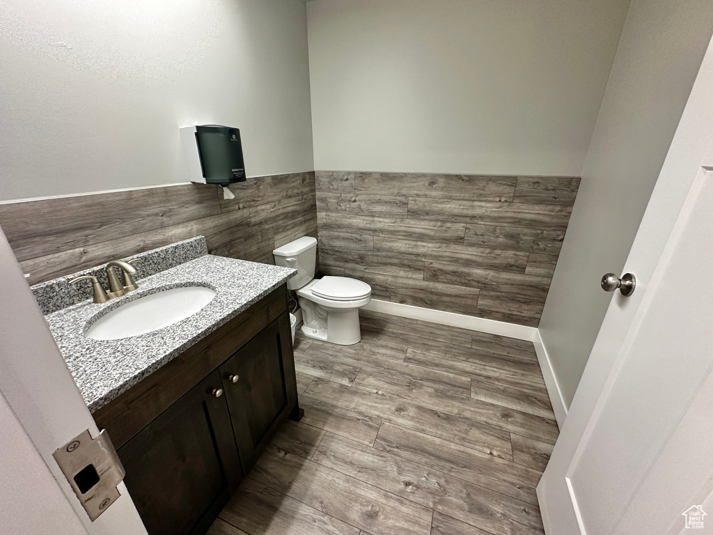 Bathroom featuring hardwood / wood-style floors, vanity, toilet, and tile walls