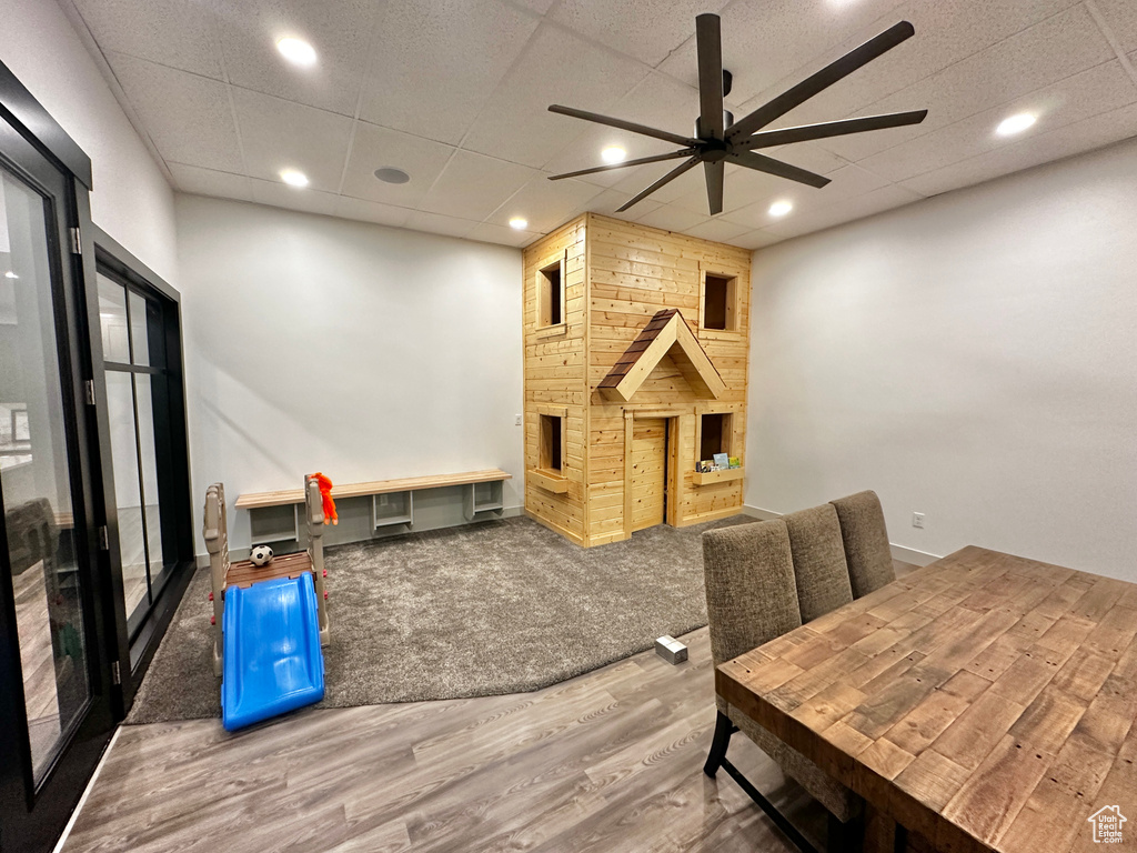 Recreation room featuring a paneled ceiling, wood walls, ceiling fan, a stone fireplace, and carpet floors