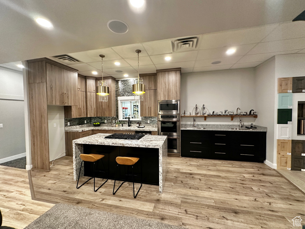 Kitchen featuring light hardwood / wood-style floors, a paneled ceiling, a kitchen island, and pendant lighting