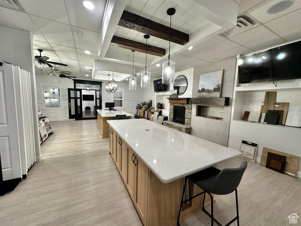 Kitchen featuring a stone fireplace, ceiling fan with notable chandelier, a large island, and light wood-type flooring