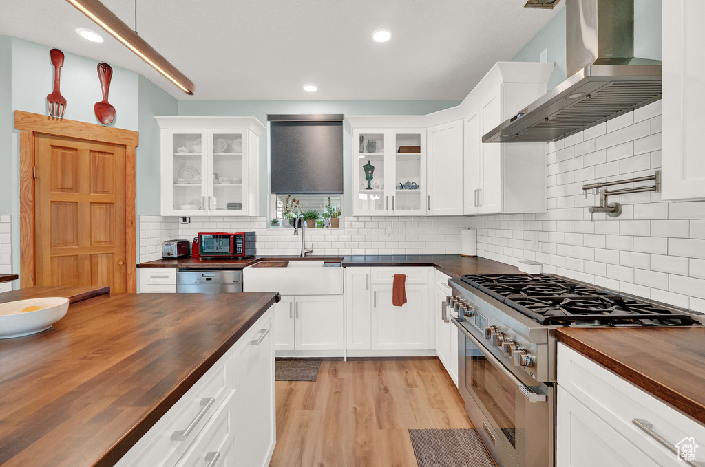 Kitchen with wall chimney range hood, double oven range, wood counters, and tasteful backsplash