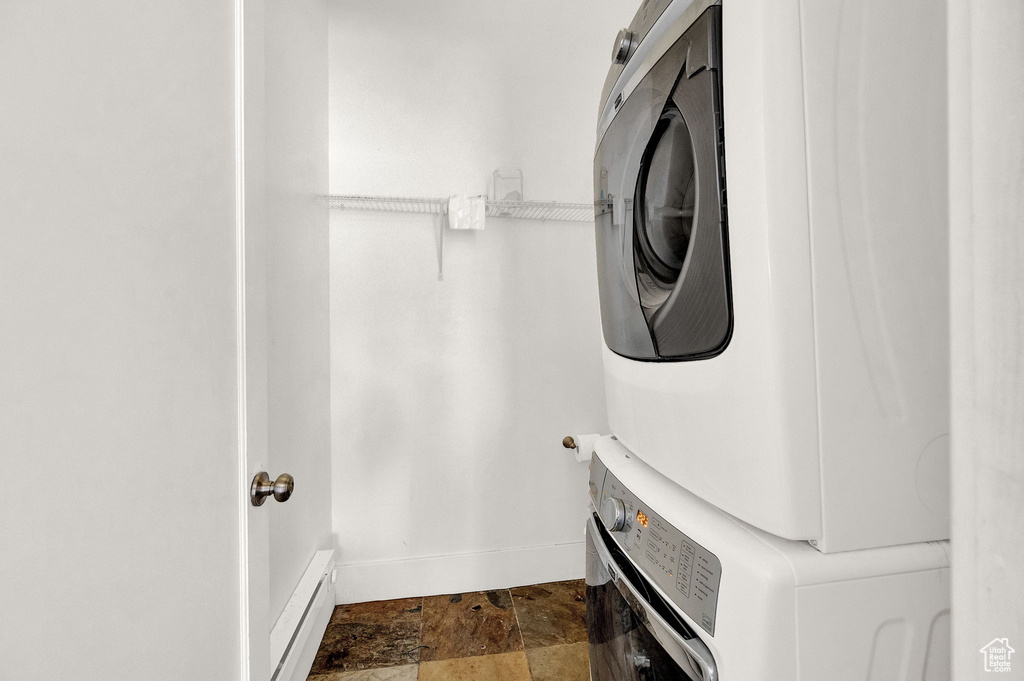 Clothes washing area with dark tile flooring and stacked washer and clothes dryer