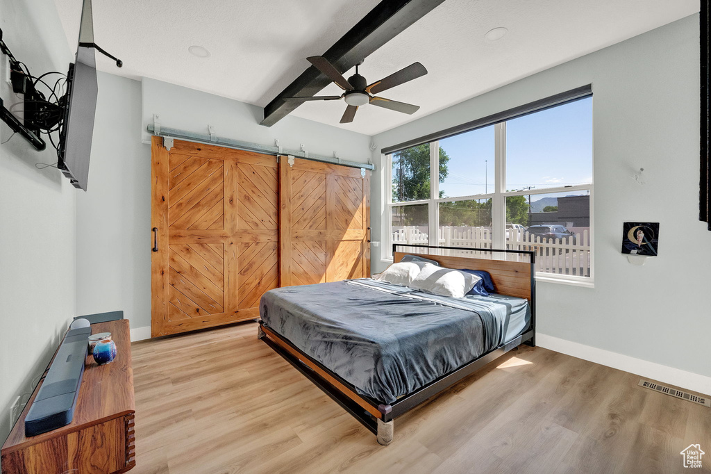 Bedroom with a barn door, beam ceiling, hardwood / wood-style flooring, and ceiling fan