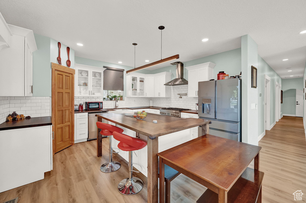 Kitchen featuring wall chimney range hood, light hardwood / wood-style flooring, backsplash, and appliances with stainless steel finishes