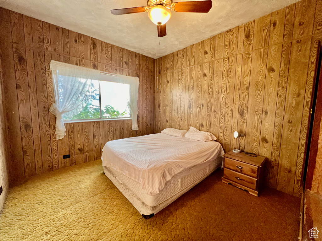 Carpeted bedroom with wood walls and ceiling fan