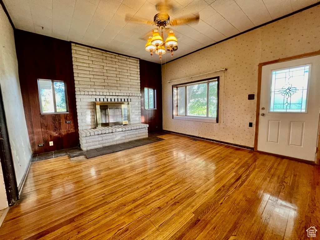 Unfurnished living room featuring light hardwood / wood-style floors, brick wall, a brick fireplace, and ceiling fan